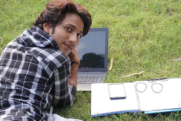 Junger Mann im Gras liegend mit Laptop